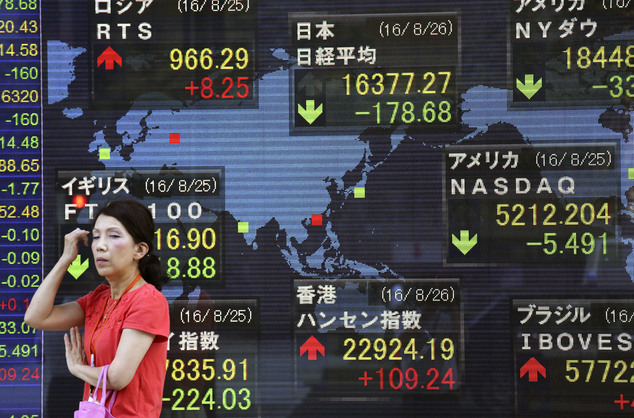 A woman stands in front of an electronic stock board of a securities firm in Tokyo Friday Aug. 26 2016. Asian stock markets were mixed Friday with invest