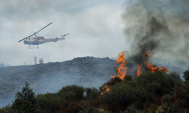 A water dropping helicopter heads back to get more water as a wildfire burns near homes in the brush in Beaumont Calif. Tuesday Aug. 30 2016. (Terry Pier