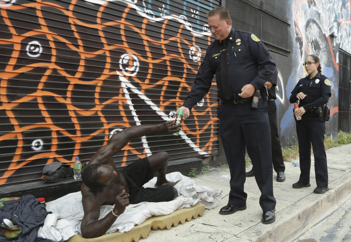 Miami police officer James Bernat right hands a can of insect repellent to a homeless man on Tuesday in the Wynwood neighborhood of Miami. The CDC has advised pregnant women to avoid travel to this neighborhood where mosquitoes are apparently transmitti