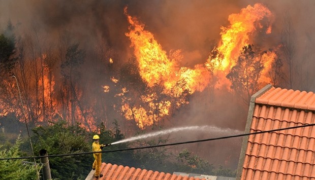 A firefighter stands on a roof of a house and tries to extinguish a wildfire at Curral dos Romeiros