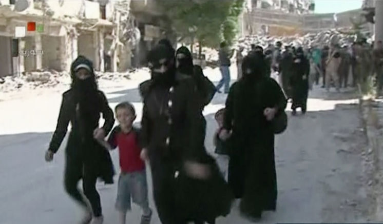 This still image from Syrian state TV video shows women and children arriving in a street lined with heavily damaged buildings in the government-held part of the Salaheddine neighborhood of Aleppo Syria Saturday