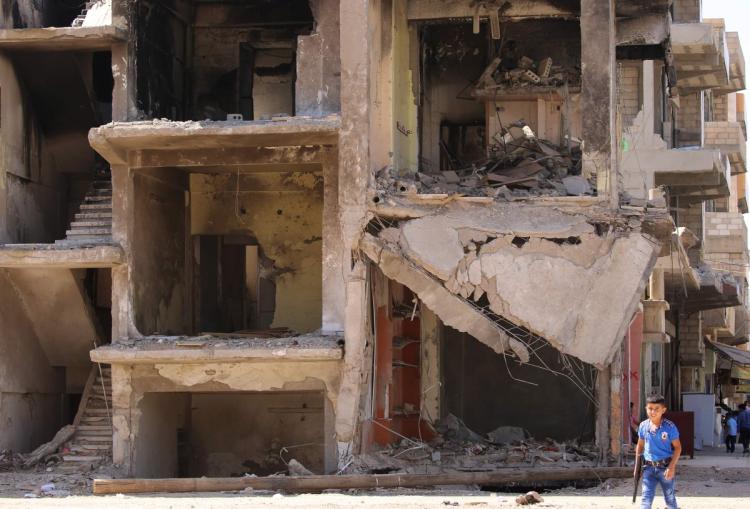 A Syrian boy carries a toy gun past a destroyed building in the northeastern Syrian city of Qamishli on Sept. 13