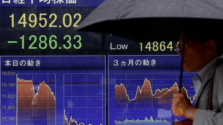 A man walks past a screen displaying the Nikkei average outside a brokerage in Tokyo Japan