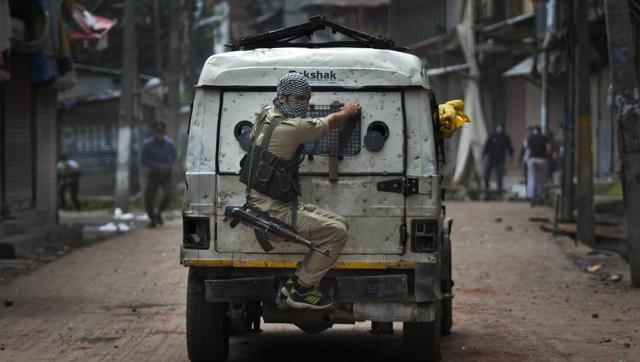 A police officer takes cover behind an armoured vehicle as Kashmiri protesters throw stones at him during a protest in Srinagar on August 30