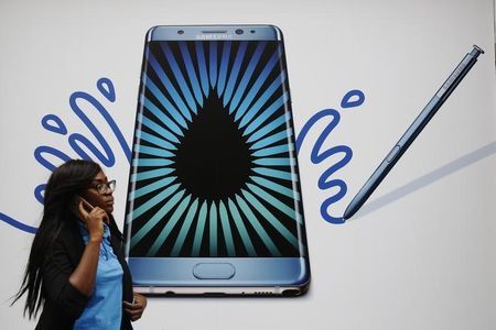 A woman speaks on a phone as she passes an advert for the Samsung Galaxy Note 7 in London