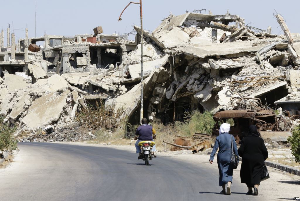 Syrians walk and drive past destroyed buildings in the government held Jouret al Shiah neighborhood of the central Syrian city of Homs