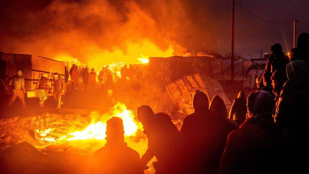 Migrants stand next to burning shacks in the southern part of the “Jungle” migrant camp in Calais