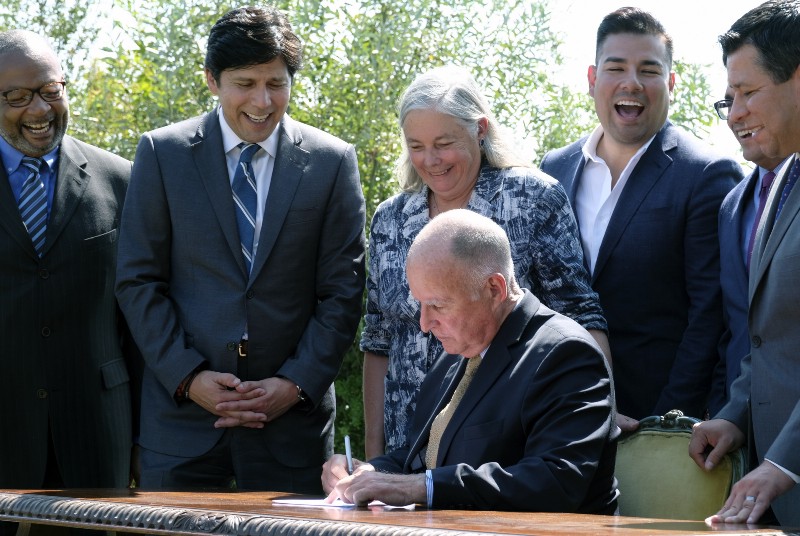 California Gov. Jerry Brown seated signs legislation