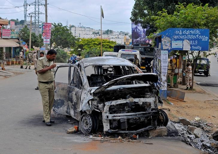 A police officer inspects the charred remains of a car set ablaze in Bengaluru following violent protests after Supreme Court ordered Karnataka to release water from the Cauvery river to the neighbouring state of Tamil Nadu India