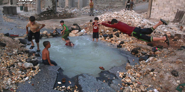 Syrian boys diving into a hole filled with water that was caused by a missile attack in the rebel-held neighbourhood of Sheikh Saeed in Aleppo province Syria