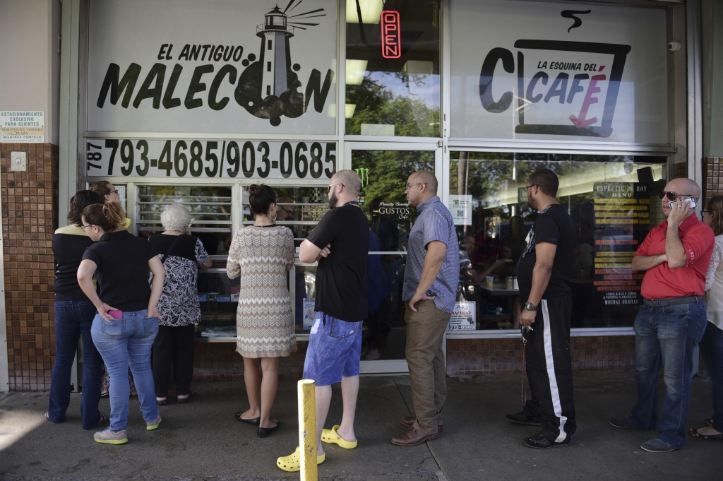 Customers stand in line at one of the few open cafeterias on Roosevelt Avenue in San Juan Puerto Rico on Thursday