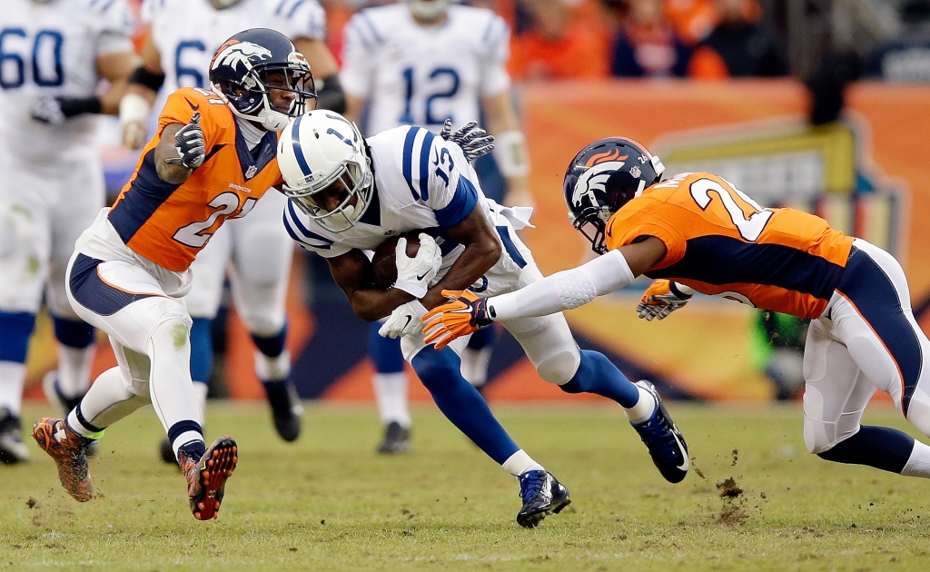 T.Y. Hilton #13 of the Indianapolis Colts carries the ball after a catch as Aqib Talib #21 and Rahim Moore #26 of the Denver Broncos defend during a 2015 AFC Divisional Playoff game at Sports Authority Field at Mile High