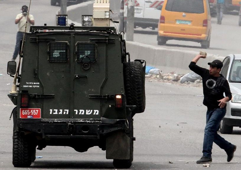 Palestinian protesters throw stones at an Israeli military car during a rally at the Qalandiya checkpoint north of Jerusalem