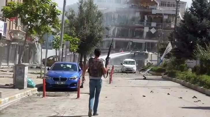 An armed policeman walks as a water cannon sprays in front of damaged buildings and vehicles after suspected Kurdish militants detonated a car bomb near local government offices in Turkey's southeastern city of Van