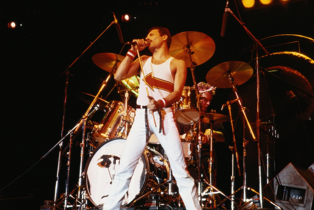 Freddie Mercury, singer with Queen standing in front of a drumkit as he sings into a microphone on stage during a live concert performance by the band at the National Bowl in Milton Keynes England United Kingdom on 5 June 1982