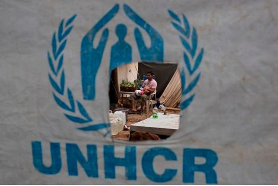 A Syrian man feeds his child behind a UNHCR plastic sheet at Ritsona refugee camp north of Athens which hosts about 600 refugees and migrants on Thursday Sept. 8 2016. The refugee crisis is expected to be a central issue in discussions Friday at a mee