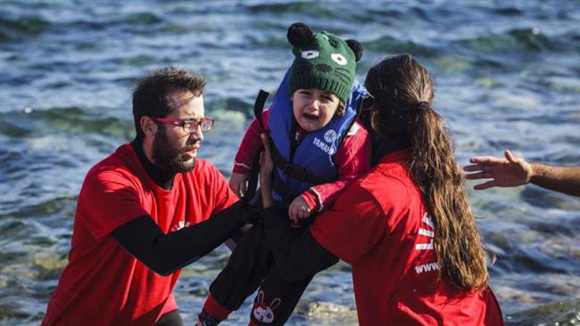 Greek lifeguards help a refugee child out of a boat that reached the shores of Lesbos having crossed the Aegean Sea from Turkey