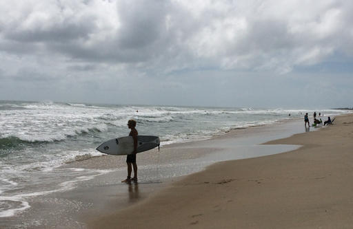 A surfer watches waves at the beach in Frisco on the Outer Banks N.C. Tuesday Aug. 30 2016. Crowds thinned Tuesday on the beaches of North Carolina's Outer Banks ahead of a tropical weather system that threatened to bring strong winds and heavy