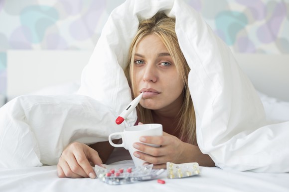 Woman Sick In Bed Flu Thermometer Medicine Getty