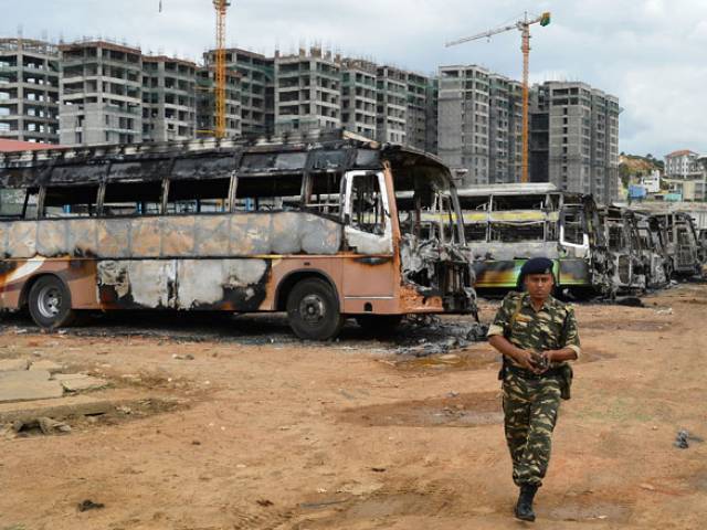 A security personnel walks past the skeletal remains of Karnataka state transport buses following violence due to the Cauvery water dispute in Bangalore