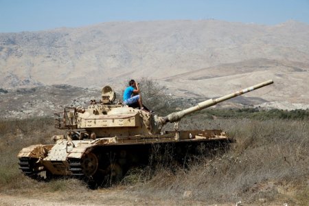 A man sits on an old tank as he watches fighting taking place in Syria as seen from the Israeli side of the border fence between Syria and the Israeli-occupied Golan Heights