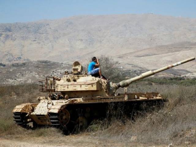 A man sits on an old tank as he watches fighting taking place in Syria as seen from the Israeli side of the border fence between Syria and the Israeli-occupied Golan Heights