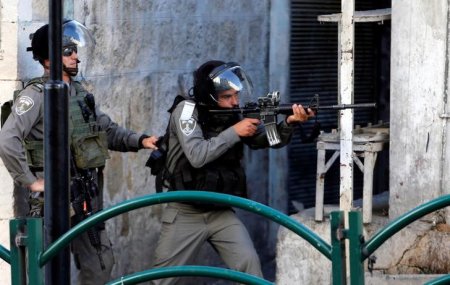 An Israeli border policeman aims his weapon towards Palestinian protesters during clashes in the West Bank city of Hebr