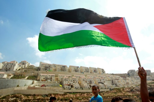 A Palestinian protester waves a national flag in front of the Israeli settlement of Beitar Illit, near the West Bank village of Wadi Fukin