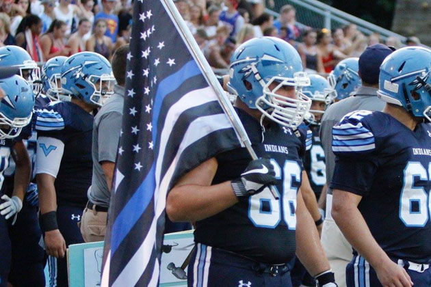 Jake Pluta of Wayne Valley High School carries a'thin blue flag onto the field