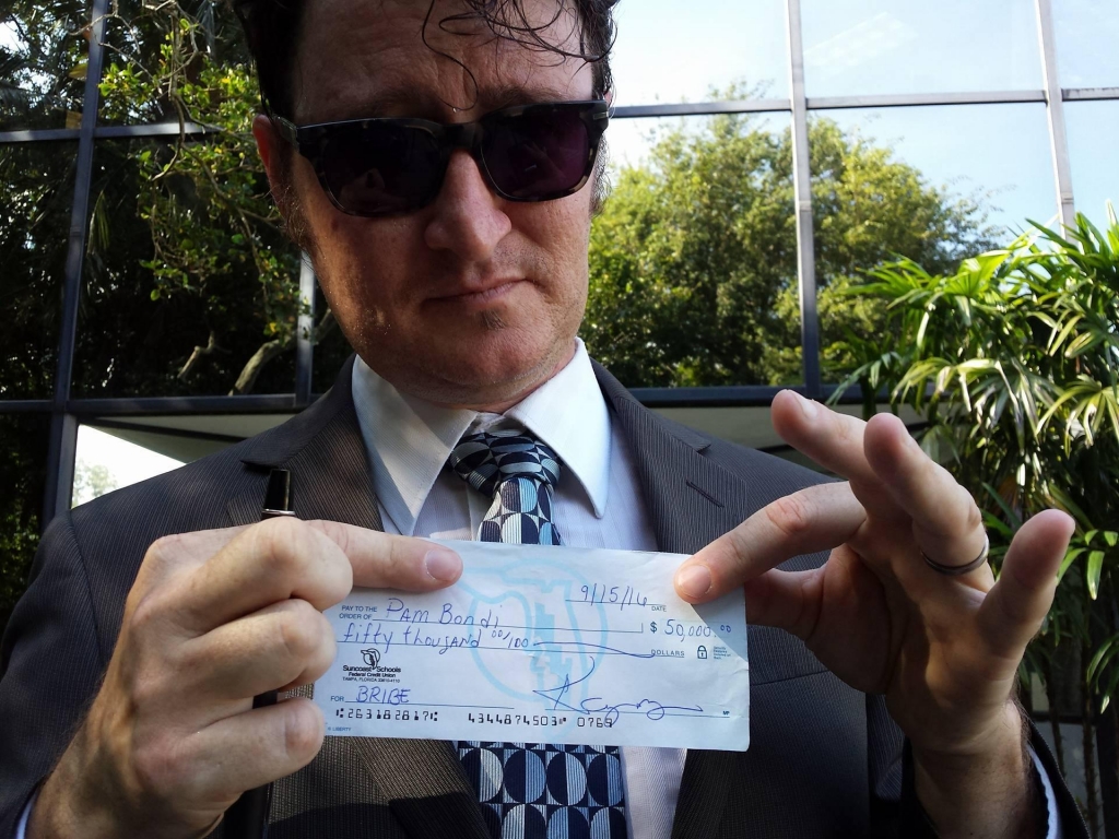 Kelly Benjamin holds a check made out to Pam Bondi for $50,000