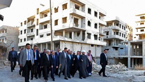 Syrian President Bashar Assad centre walks with officials througha destroyed neighbourhood in Daraya after morning