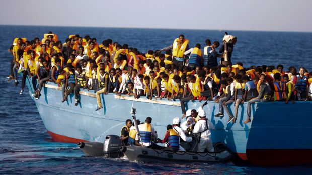 Italian officers rescue a woman from a crowded wooden boat carrying more than seven hundred migrants during a rescue