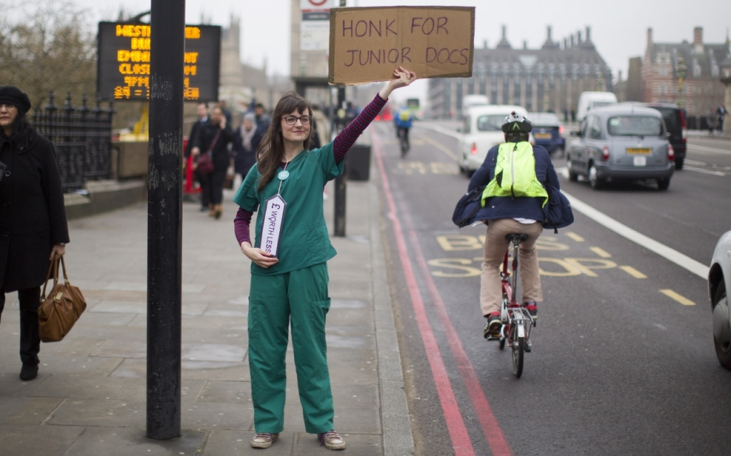 A junior doctor on Westminster Bridge holding a'honk for junior docs sign