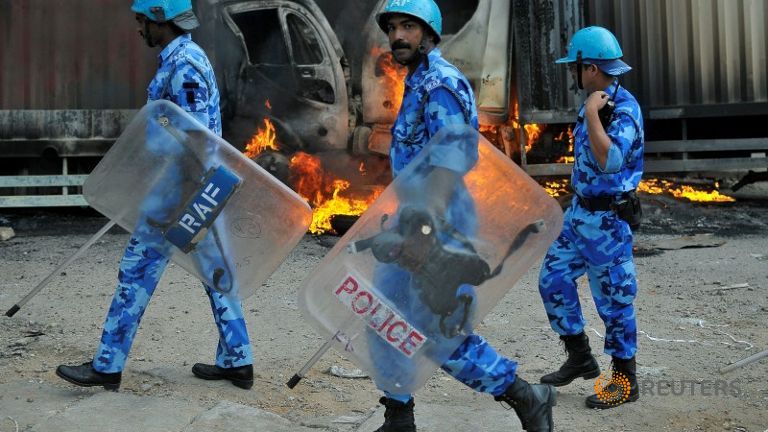 Members of the security forces make their way past burning lorries in Bengaluru     
   Enlarge  Caption