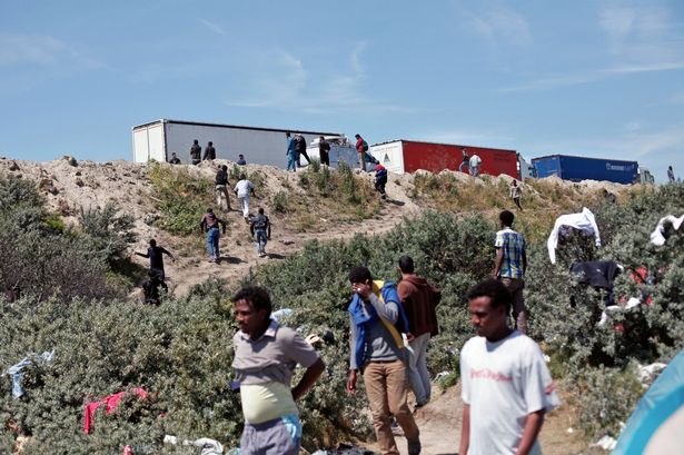 Migrants stand along a motorway leading to a ferry port to cross the English Channel in Calais