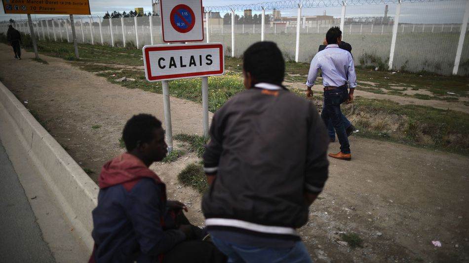 Migrants walk past security fencing at the Jungle migrant camp in Calais