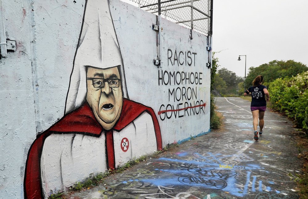 A jogger passes a wall with graffiti depicting Gov. Paul Le Page in a Ku Klux Klan robe along the Eastern Promenade Trail in Portland Tuesday. The wall is owned by the Portland Water District and part of the wastewater treatment plant