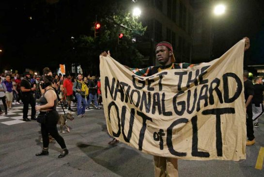 A protester holds a banner against the North Carolina National Guard as he marches in the streets of Charlotte N.C. Friday Sept. 23 2016 over Tuesday's fatal police shooting of Keith Lamont Scott