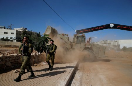 Israeli army soldiers keep guard as an Israeli military front loader opens the entrance of the West Bank village of Bani Na'im near Hebr