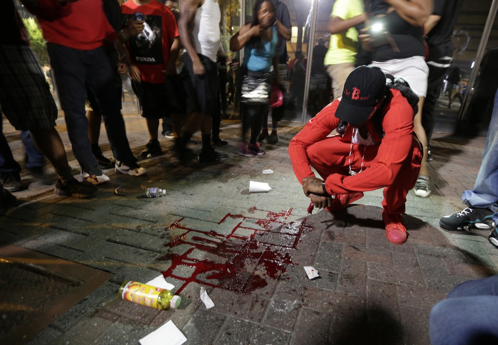 A man squats near a pool of blood after a man was injured during a protest of Tuesday's fatal police shooting of Keith Lamont Scott in Charlotte N.C. on Wednesday Sept. 21 2016. Protesters rushed police in riot gear at a downtown Charlotte hotel and