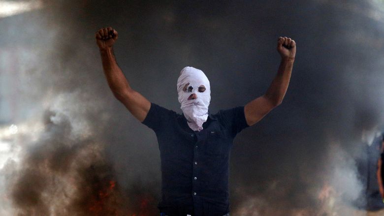 A man in a balaclava gestures in front of burning debris following a protest against the recent killings in Kashmir in Srinagar India