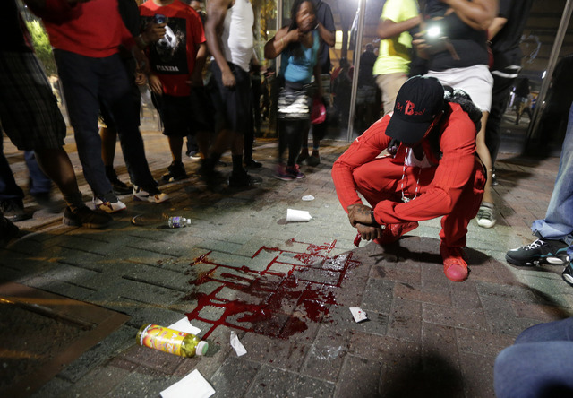 A man squats near a pool of blood after a man was injured during a protest of Tuesday's fatal police shooting of Keith Lamont Scott in Charlotte N.C. on Wednesday Sept. 21 2016. Protesters rushed police in riot gear at a downtown Charlotte hotel and