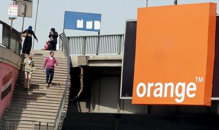 People walk past a sign of French telecom operator Orange hanging from a bridge in Cairo Egypt