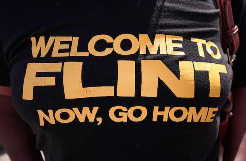 Black woman wears black shirt with yellow lettering that says'Welcome to Flint now go home