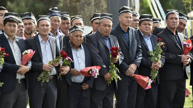 People hold flowers as they gather along the road