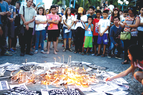 3 2016 shows people offering prayers and flower amongst lighted candles at the site of a bomb blast during a memorial service. — AFP