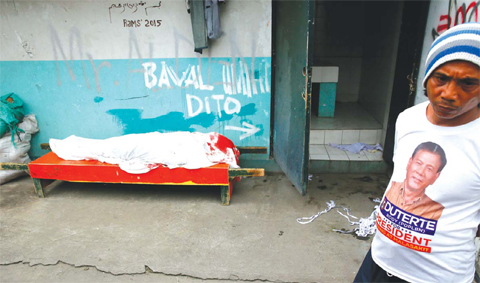 MANILA A resident wearing an election campaign t-shirt of the then Presidential candidate Rodrigo Duterte stands near the body of a Filipino Muslim which is wrapped in white cloth after he and another Muslim were killed in a police “buy-bust” opera