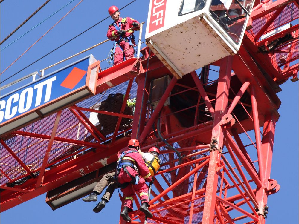 Firefighters lower a man who was at the top of a construction crane along 10th Avenue S.W. on Monday