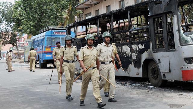 Policemen walk past a charred bus in a violence-hit Heganahalli area in Bengaluru