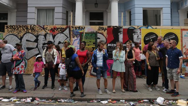 Revellers stand on the pavement in front of boarded up houses on the first day of the Notting Hill Carnival in west London on Sunday